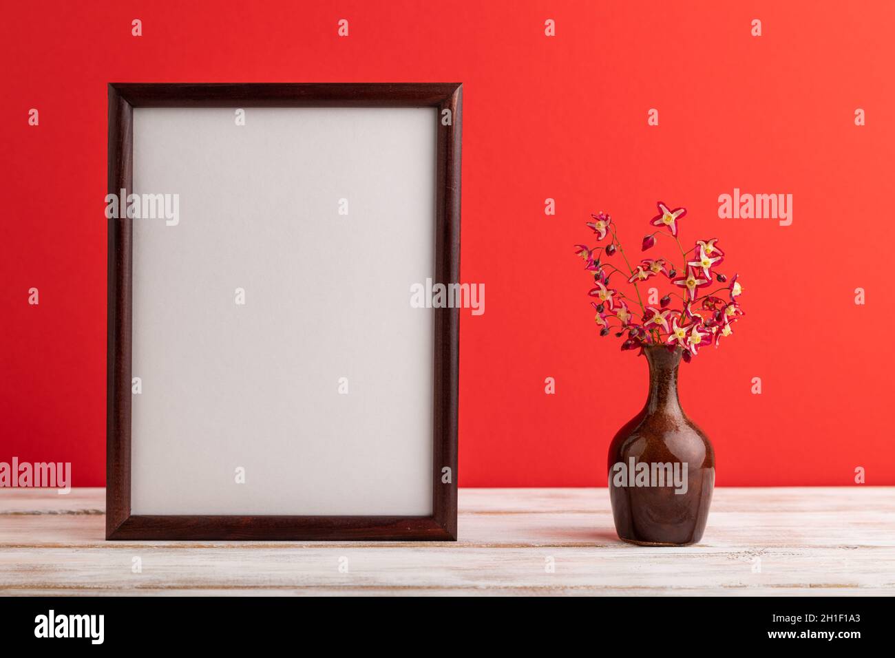 Wooden frame with purple barrenwort flowers in ceramic vase on red pastel background. side view, copy space, still life, mockup, template, spring, sum Stock Photo