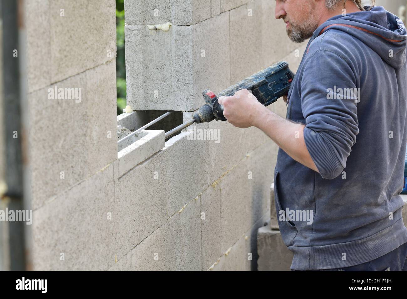 A mason on a construction site drills with a hand drill into the wall