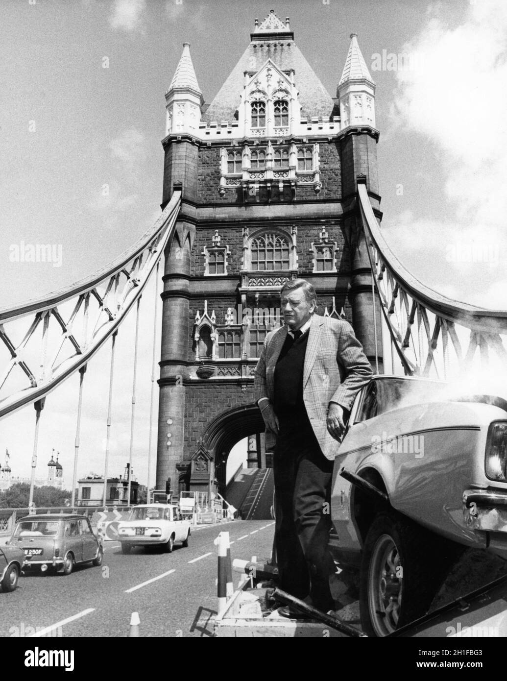 JOHN WAYNE as Chicago Police Lieutenant publicity portrait next to crashed car on Tower Bridge in London in BRANNIGAN 1975 director DOUGLAS HICKOX UK - USA co-production Wellborn / Levy - Gardner -Laven / United Artists Stock Photo