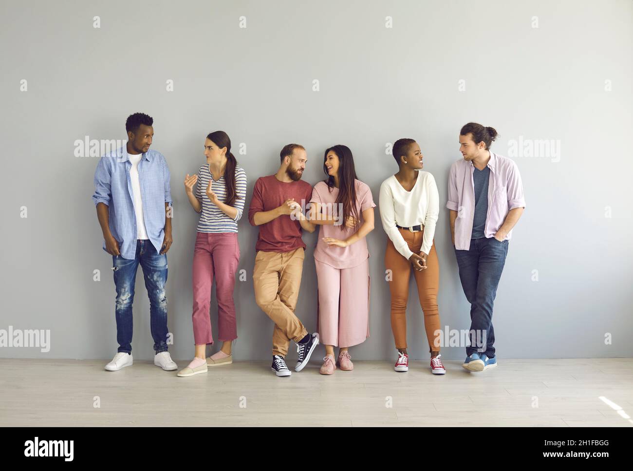 Portrait of diverse group of happy young men and women standing in studio and talking Stock Photo