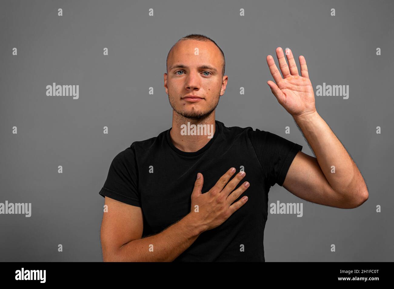 I promise to tell truth. Portrait of honest responsible man in a black shirt with one hand on his heart and the other raised making an oath, pledging Stock Photo