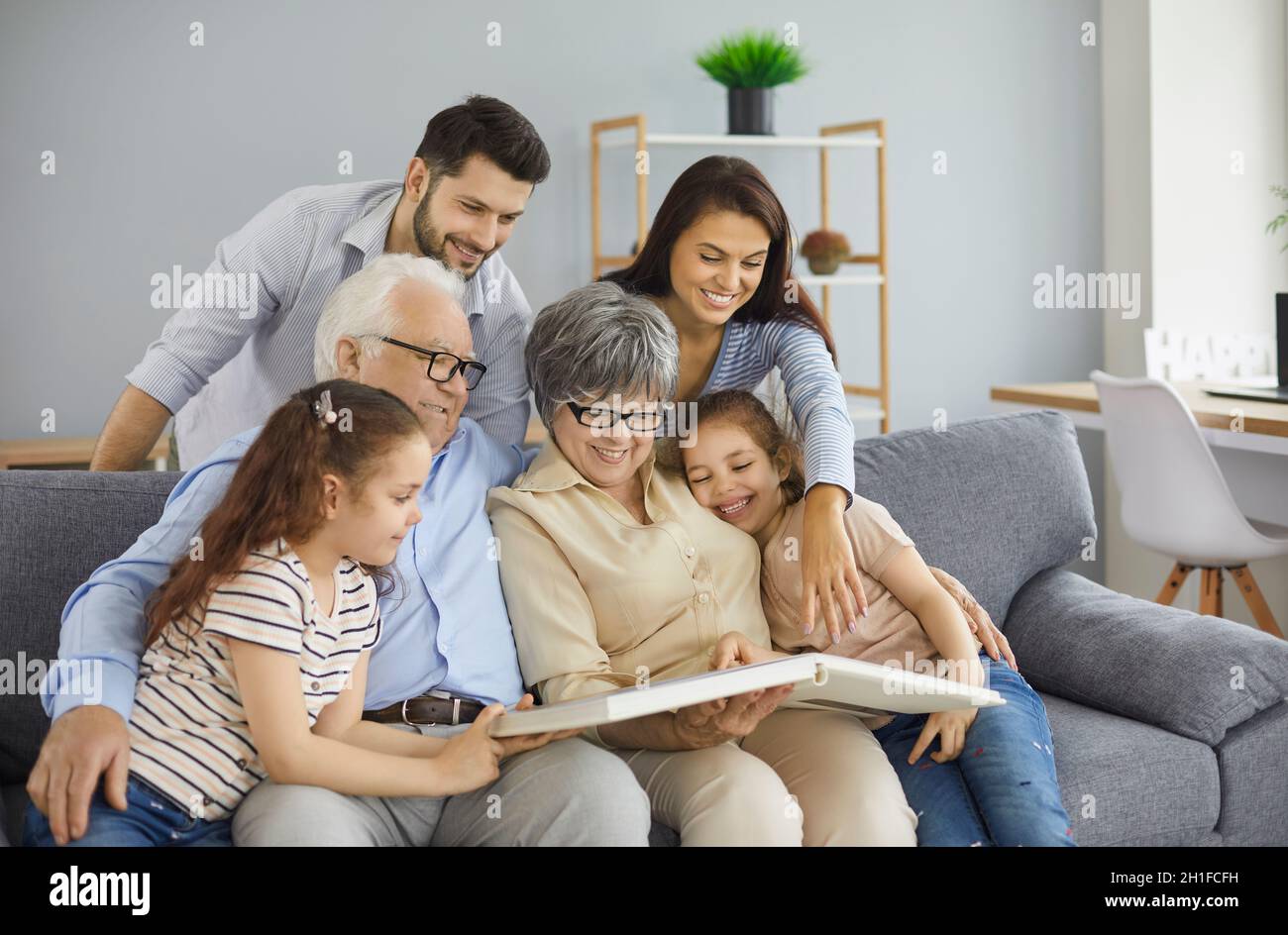 Happy family grandparents with twin granddaughters and their parents browse the family photo album. Stock Photo