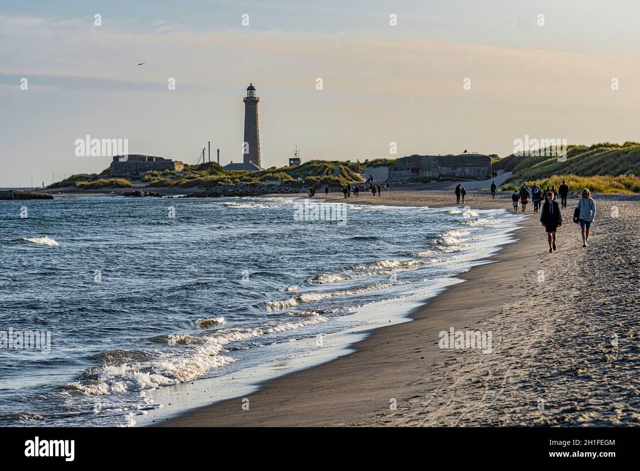 Tourists along the sandy Grenen Peninsula where the Baltic Sea meets the North Sea. In the background the Skagen lighthouse. Skagen, Denmark Stock Photo