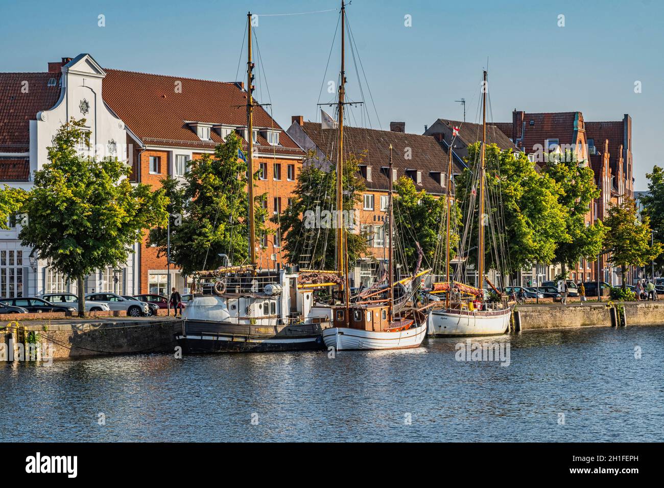 Lübeck, fishing and touring boats moored on the river Trave, houses with traditional architecture overlook the long river. Lubeck, Germany Stock Photo