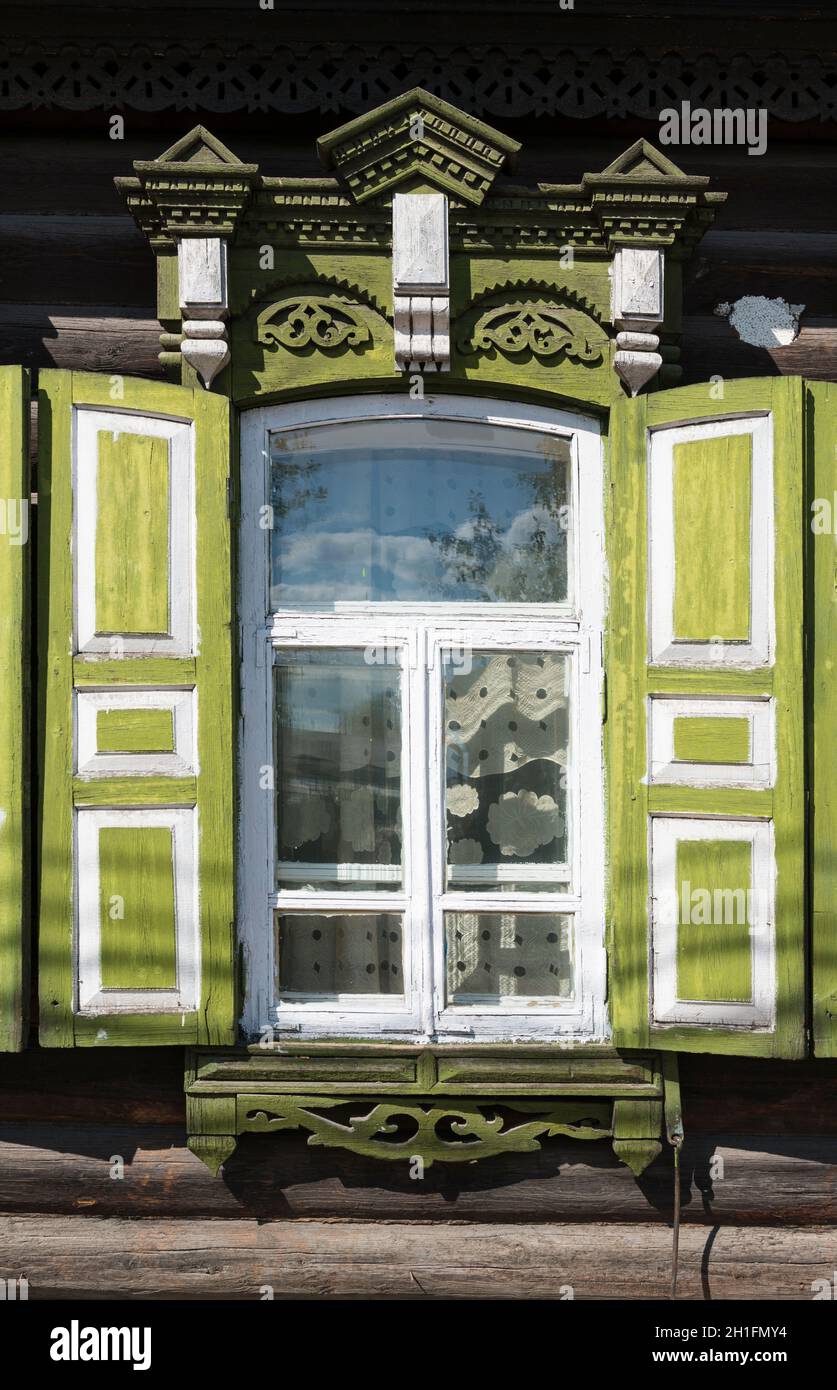 Floral pattern curtainig  behind a window with green shutters of  a traditional wooden house in Ulan-Ude. Republic of Buryatia, Russia Stock Photo