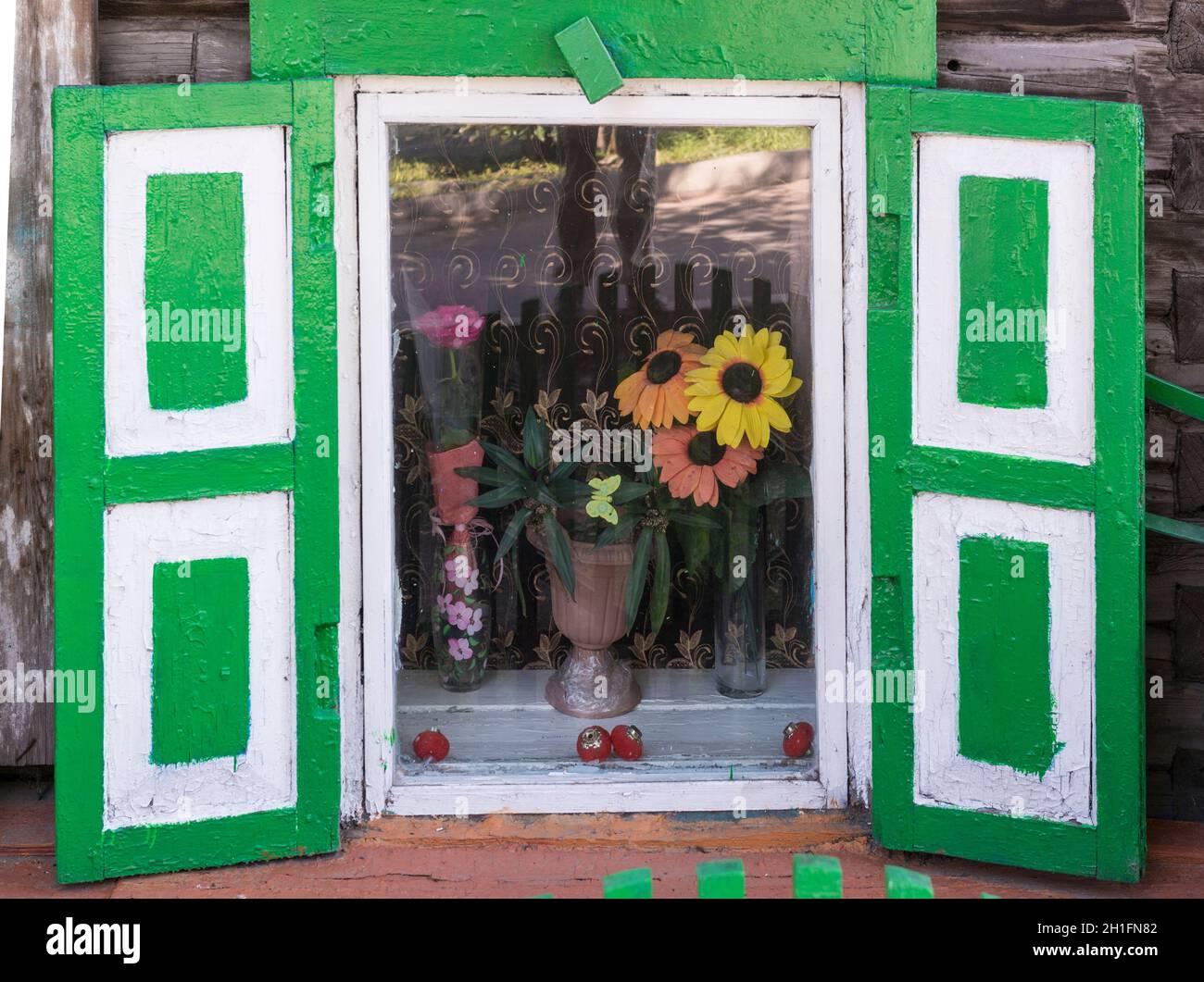 Artificial flowers behind a window with green shutters of  a traditional wooden house in Ulan-Ude. Republic of Buryatia, Russia Stock Photo