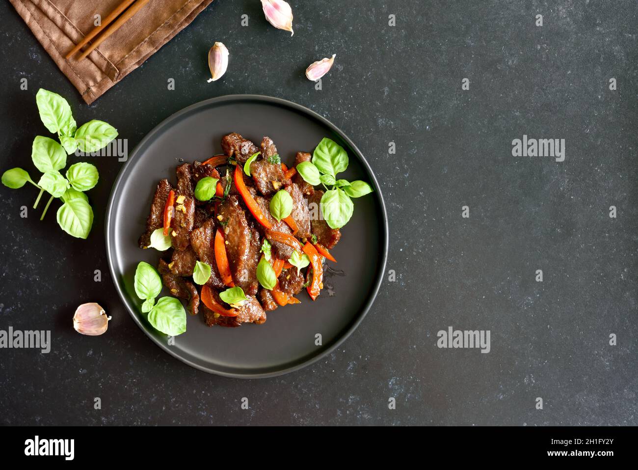 Thai beef stir-fry with pepper and basil on dark background with copy space. Top view, flat lay Stock Photo