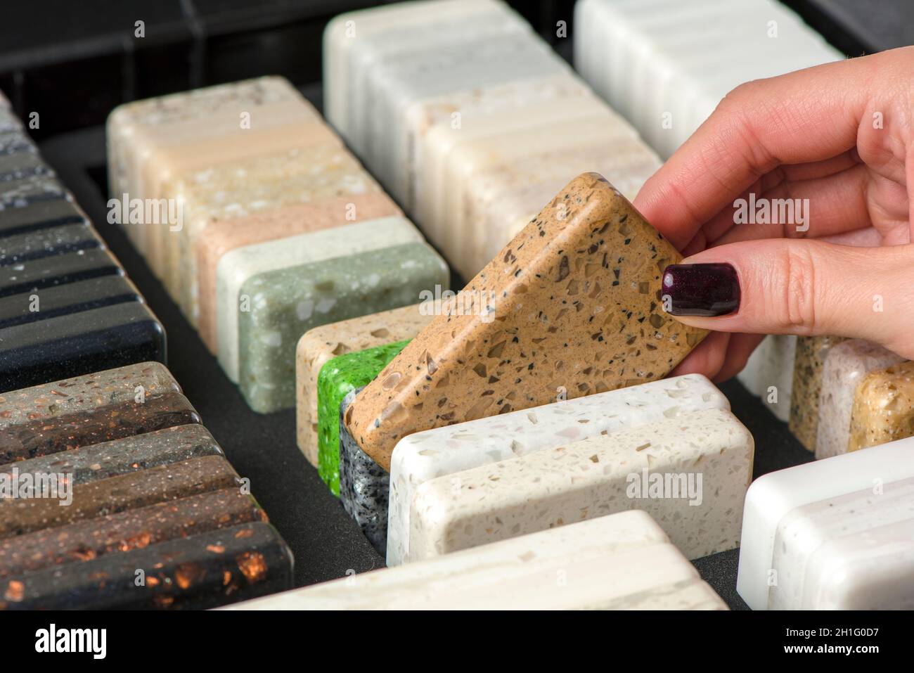 A woman chooses stone samples for a kitchen countertop. A set of multi-colored samples of artificial acrylic stone. Stock Photo