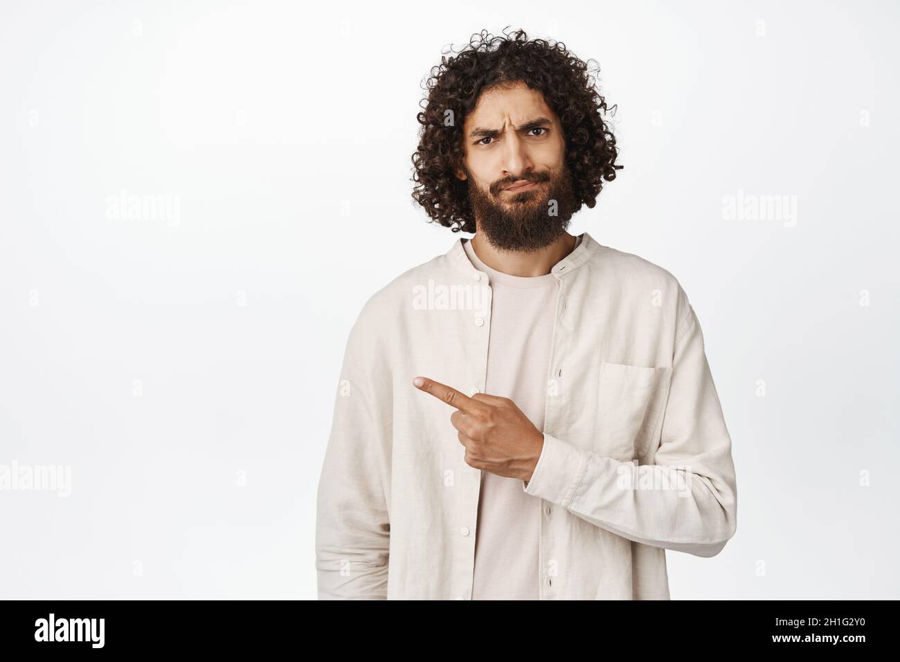 Sad and disappointed middle eastern guy pointing left, showing advertisement with upset face expression, white background Stock Photo