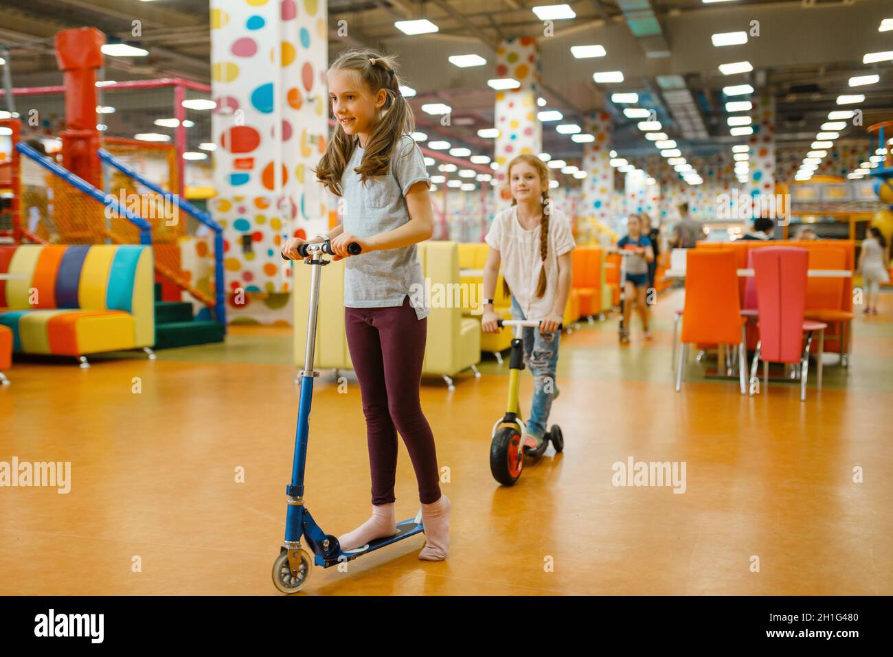 Little girlfriends rides on scooters in the entertainment center. Female children leisures on holidays, childhood happiness Stock Photo