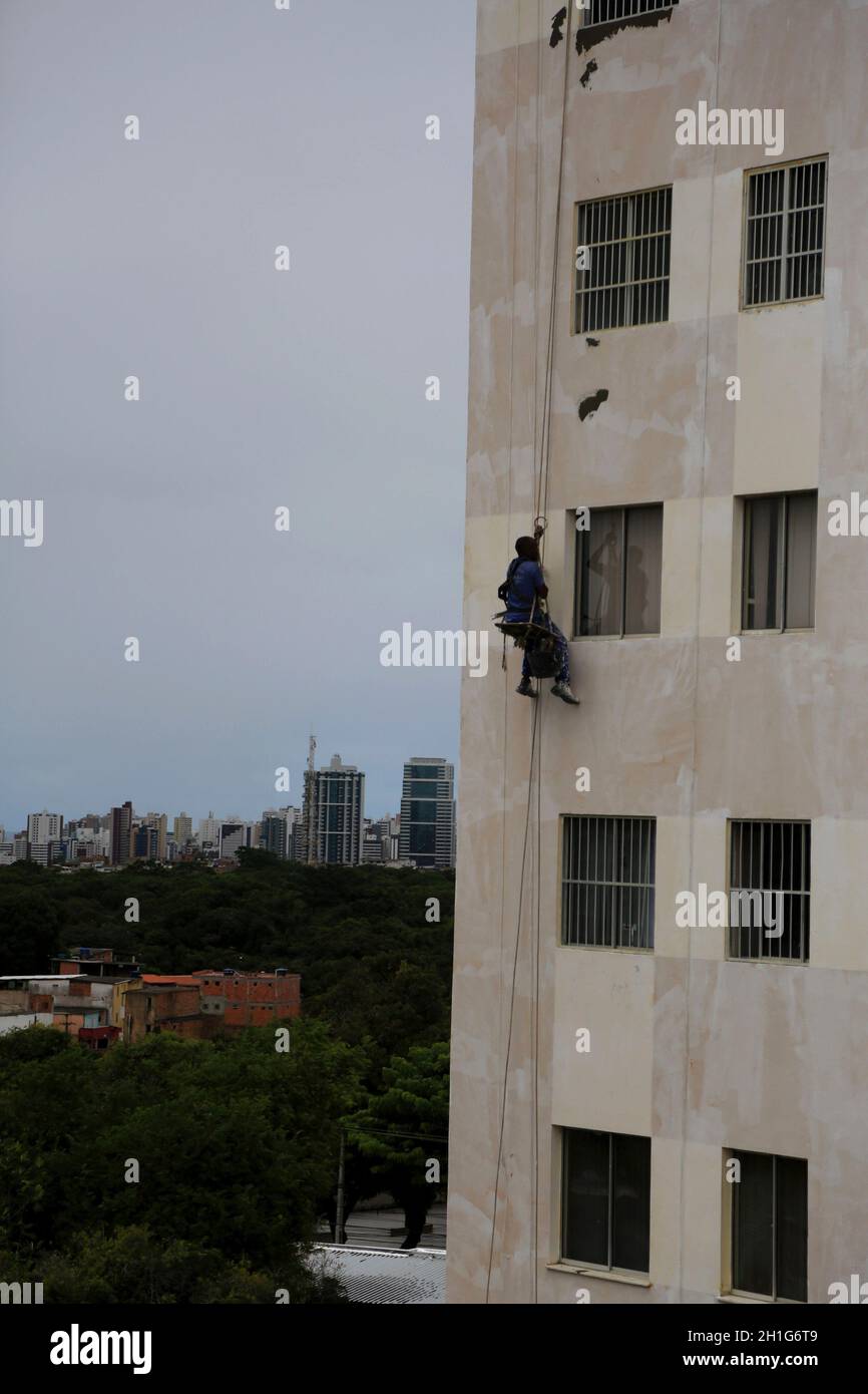 salvador, bahia - brazil - february 24, 2016: wall painter is seen working hanging from ropes on the wall of a thirteen-story building in the Cabula n Stock Photo