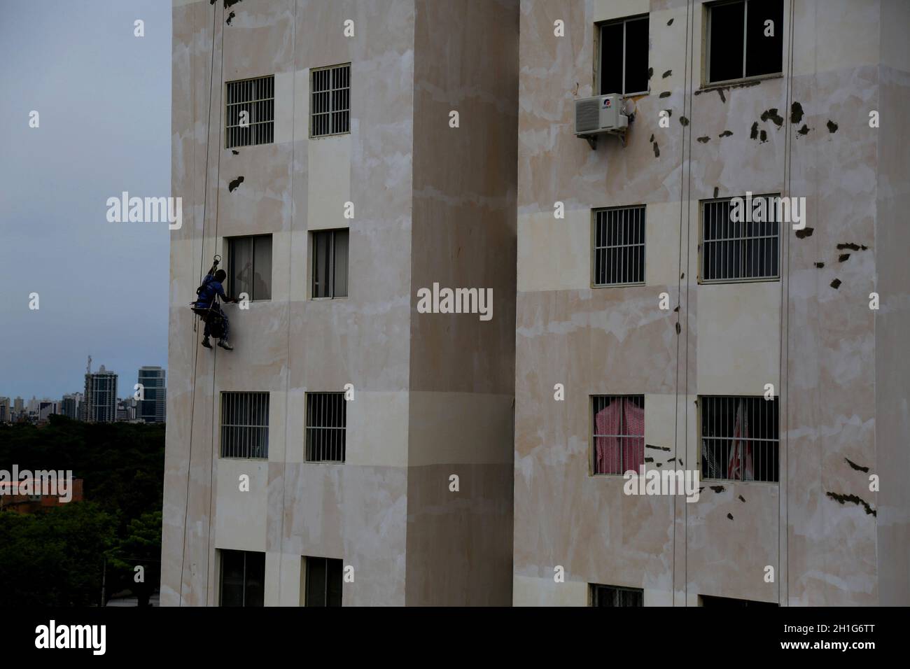 salvador, bahia - brazil - february 24, 2016: wall painter is seen working hanging from ropes on the wall of a thirteen-story building in the Cabula n Stock Photo