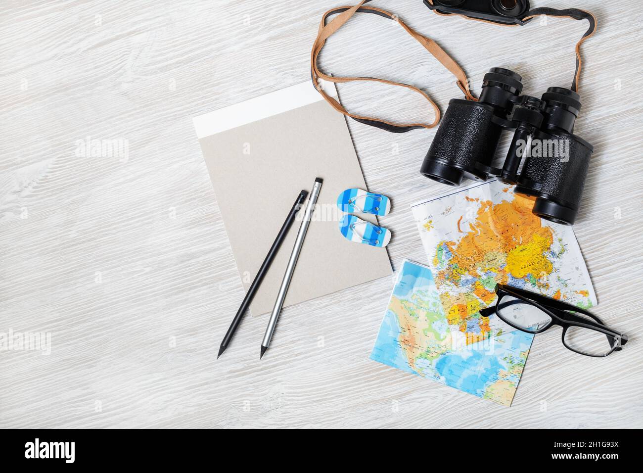 Ready for the trip. Travel plan background. Map, binoculars, notebook, glasses, pencils and flip flops on light wood table background. Flat lay. Stock Photo