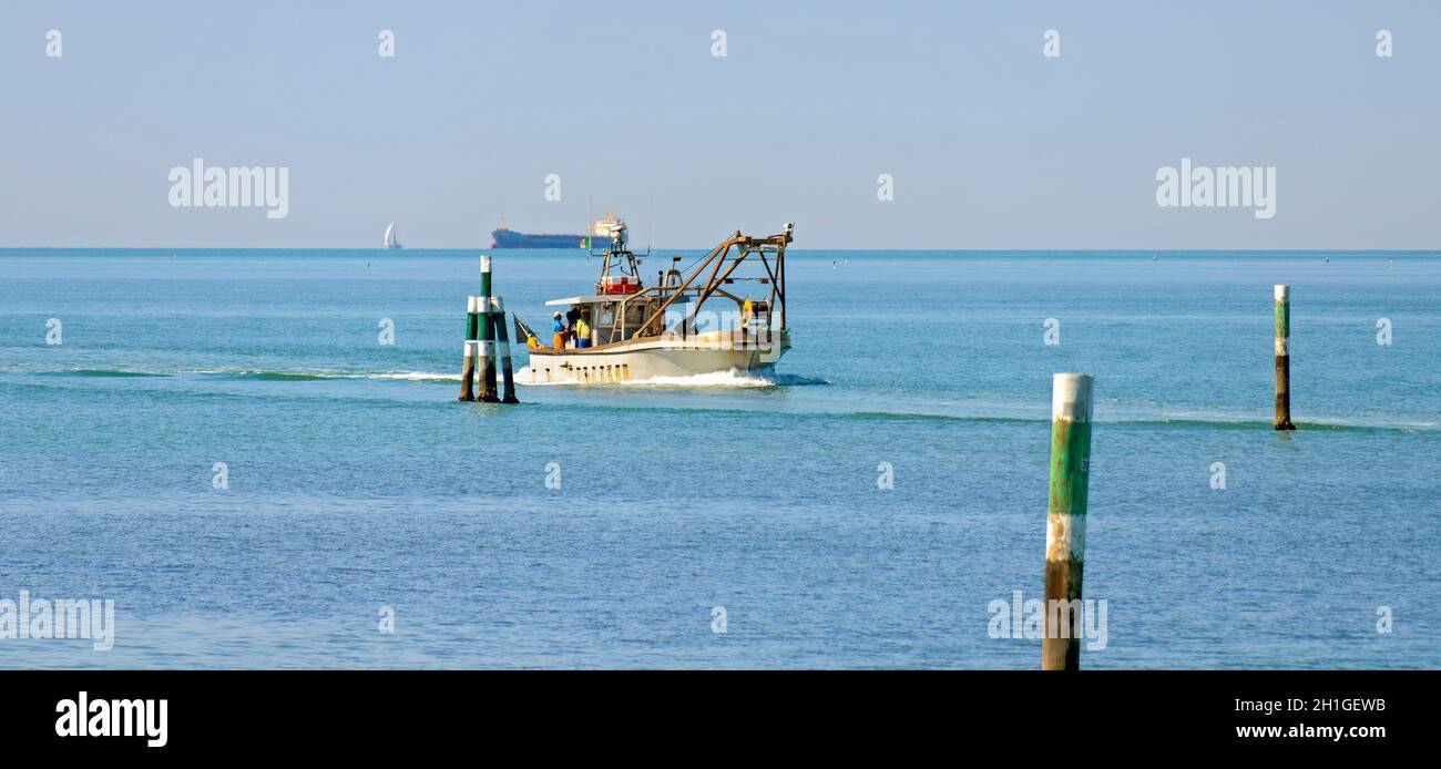 fishing ship on homeward journey between waterway marks on the upper Adriatic sea near Grado with a tank vessel on the horizon, Italy Stock Photo