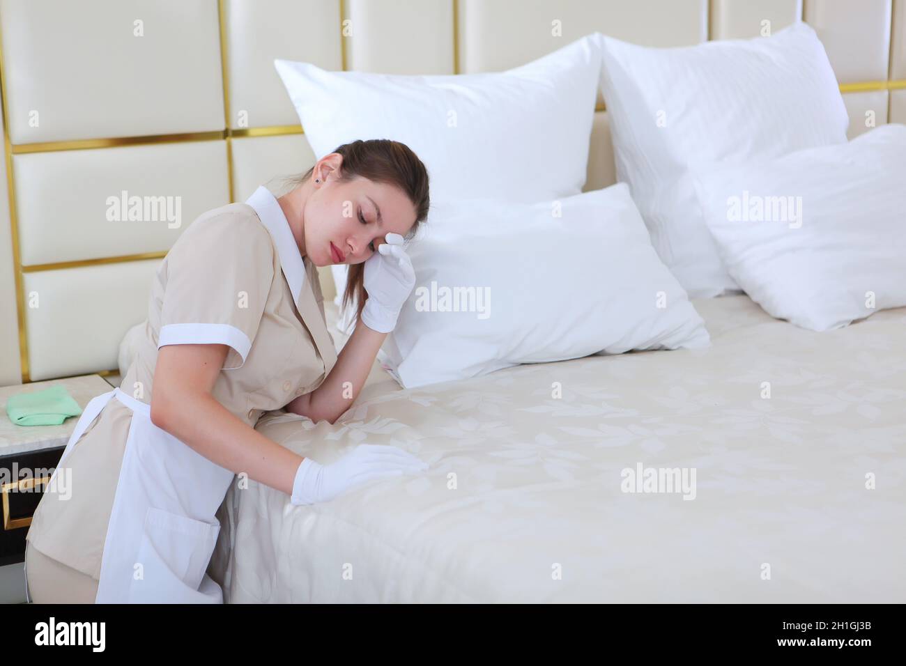 Fatigue at work.Young maid in the bedroom. Hands in white cotton gloves. The concept of cleaning. Headache. Copy space. Photo in the interior. Stock Photo
