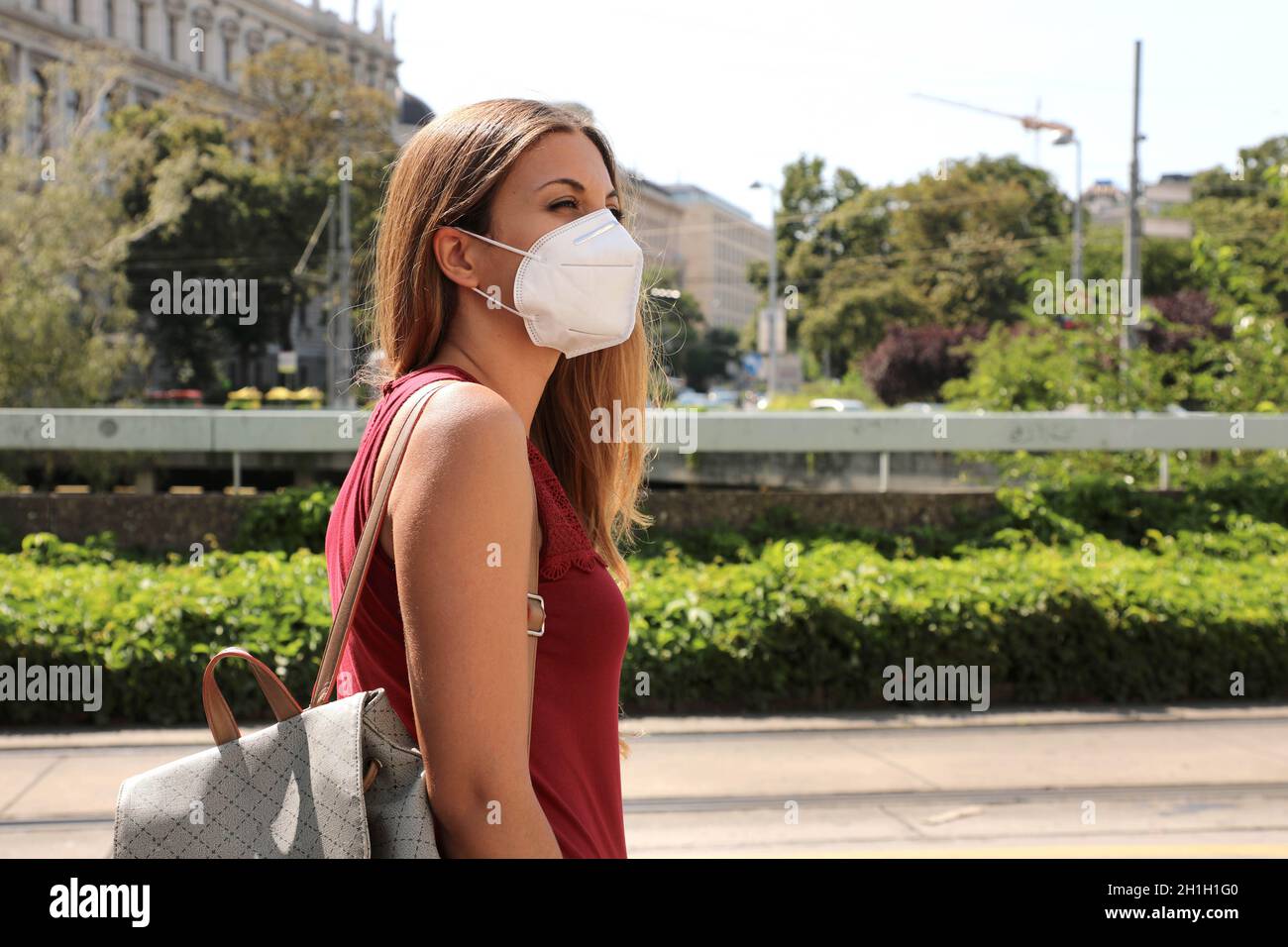COVID-19 Woman in city street wearing KN95 FFP2 mask protective for spreading of disease virus SARS-CoV-2. Girl with protective mask on face against C Stock Photo