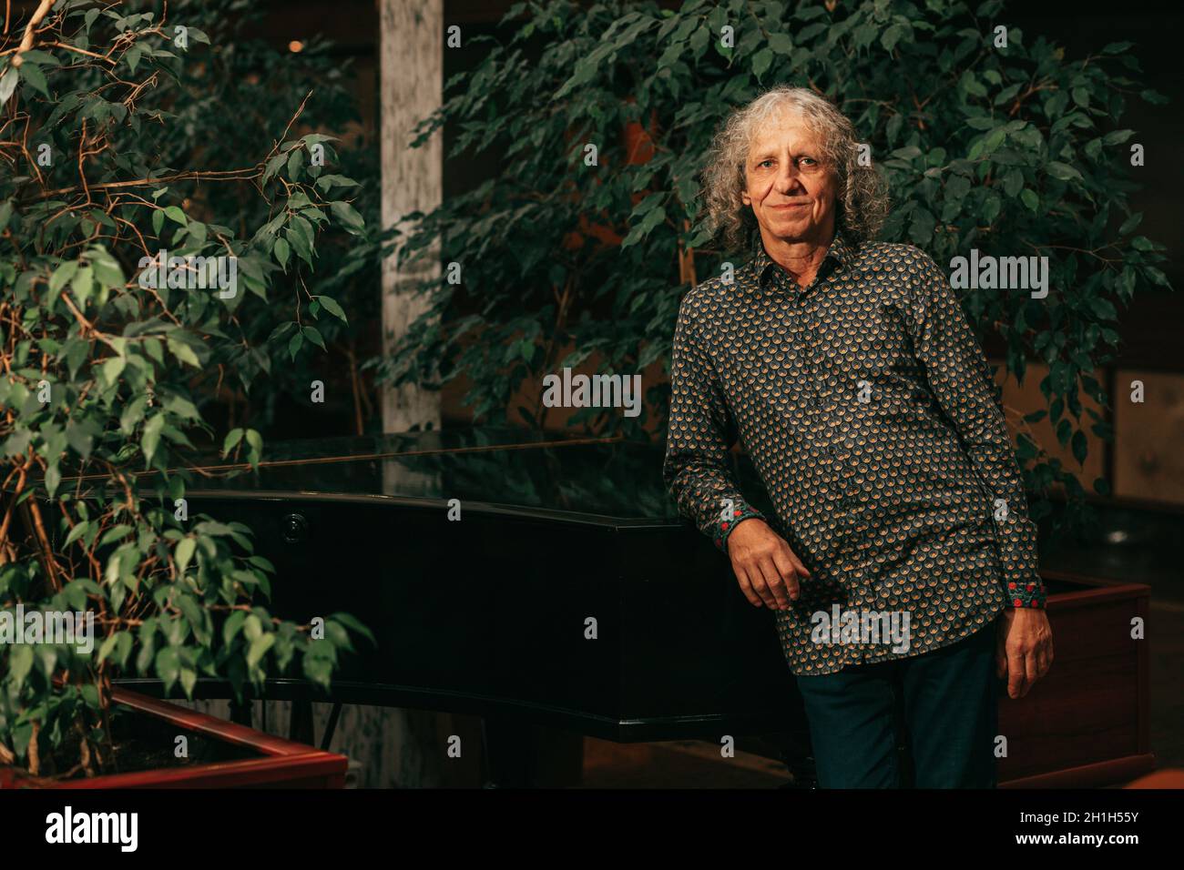 portrait of 65-year-old mature man at piano musical instrument in lobby of hotel gray curly hair, charismatic appearance. Stock Photo
