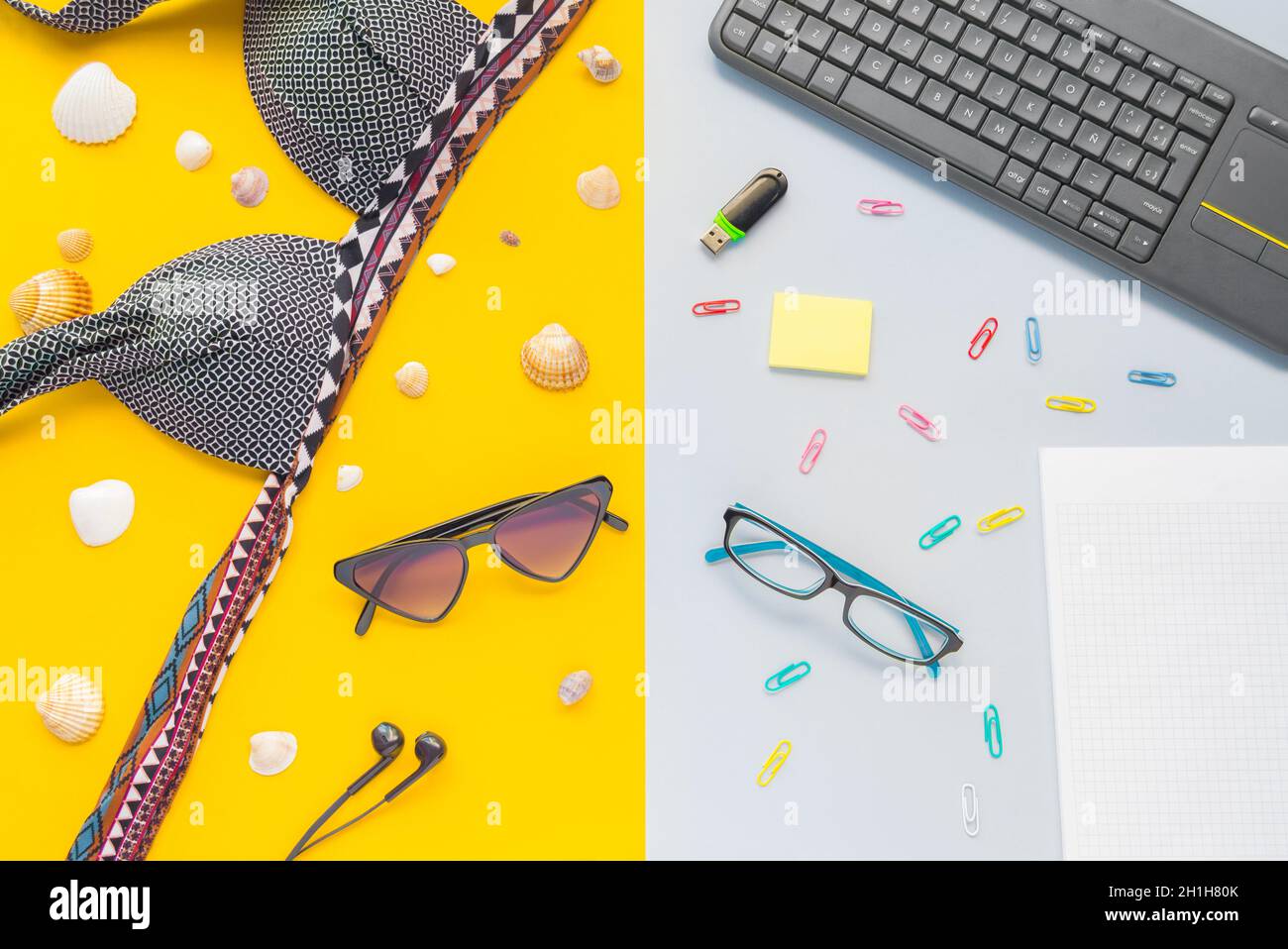 Working desk with clips, keyboard, eyewear, and bikini on a yellow and blue surface Stock Photo