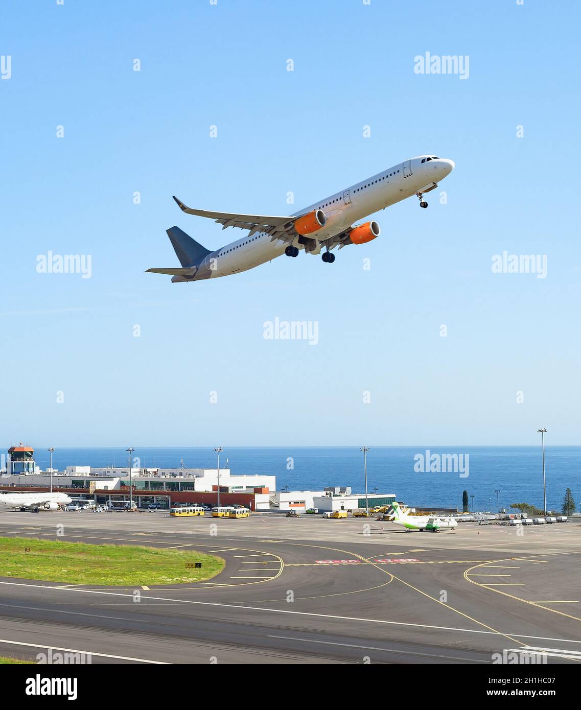 Airplaine taking off runway at Madeira international airport, terminal building and seascape in background, Portugal Stock Photo