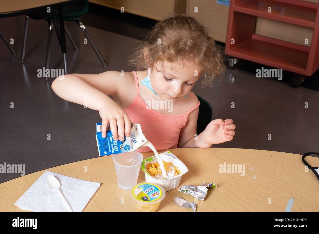 Education Preschool 4-5 year olds girl pouring own milk into her cereal at breakfast Stock Photo