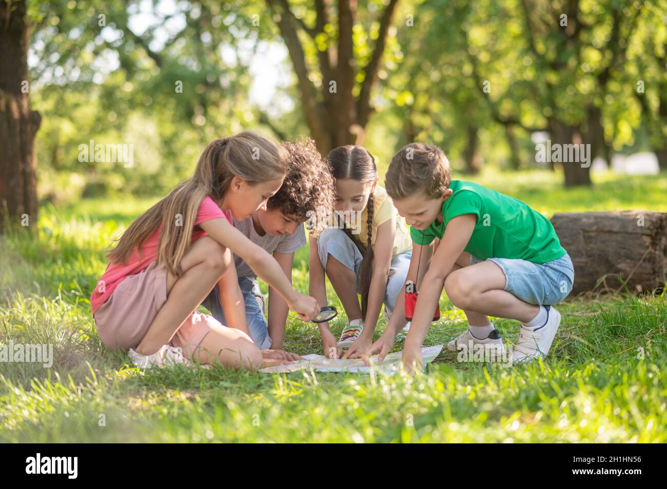 Children with map and magnifying glass on lawn Stock Photo