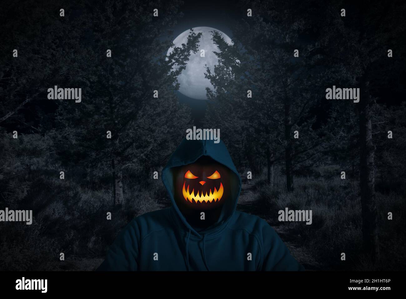 Portrait of a man with a pumpkin instead of a head standing in the dark forest with moon light. Horror Halloween concept. Stock Photo