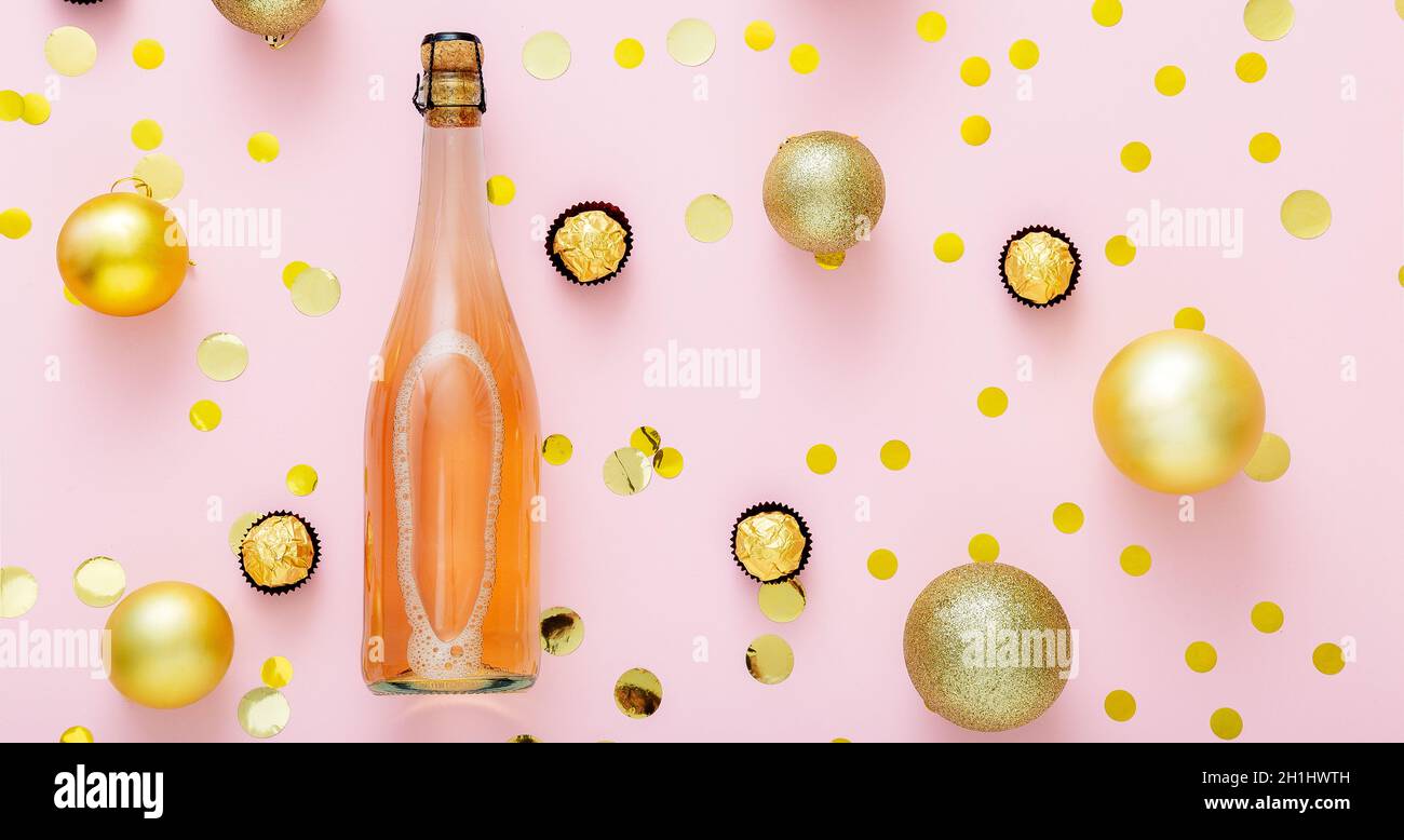 Pink champagne bottle with confetti, sweet candies and Christmas balls golden christmas decorations on pink background. Flat lay Long web banner Stock Photo