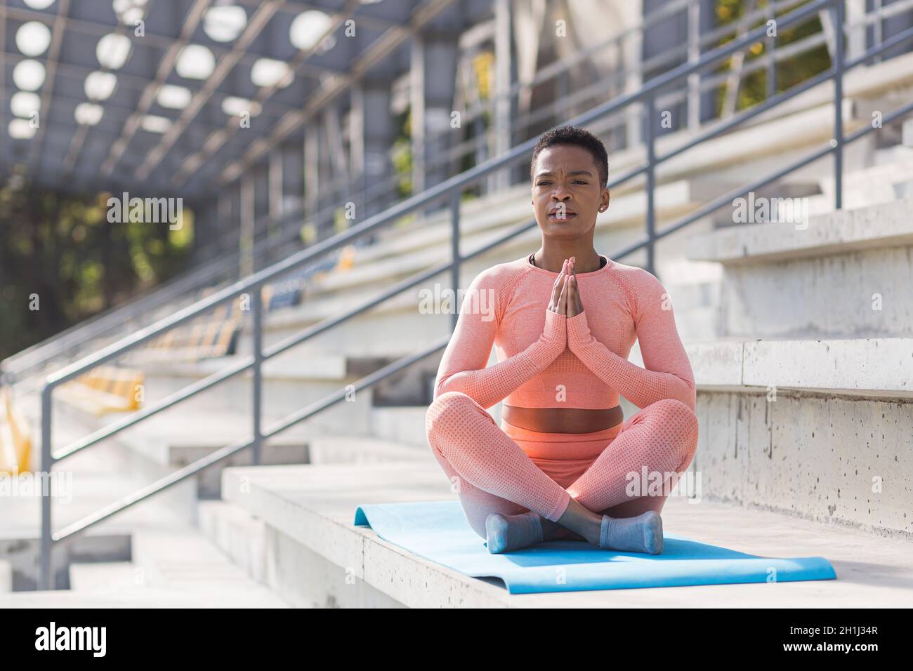 Young beautiful woman meditating in the morning, African American woman dressed in a pink sports suit performs fitness exercises with breathing, near Stock Photo