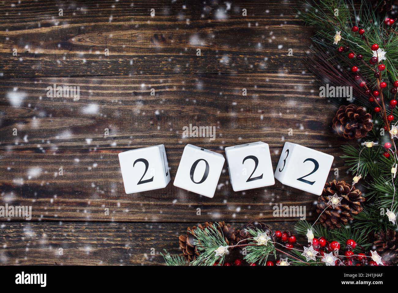 New Year's 2022 wood calendar blocks. Christmas tree lights, pine branches, red winter berries and snow. Top view with copy space available. Stock Photo