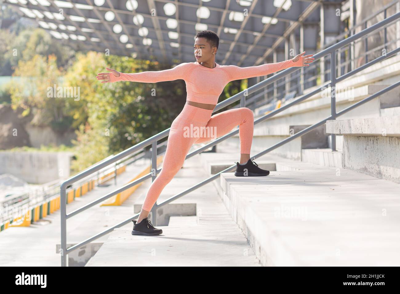 Female athlete doing fitness in a pink sports suit near the sports stadium, African American performs fitness exercises and stretching in the morning Stock Photo