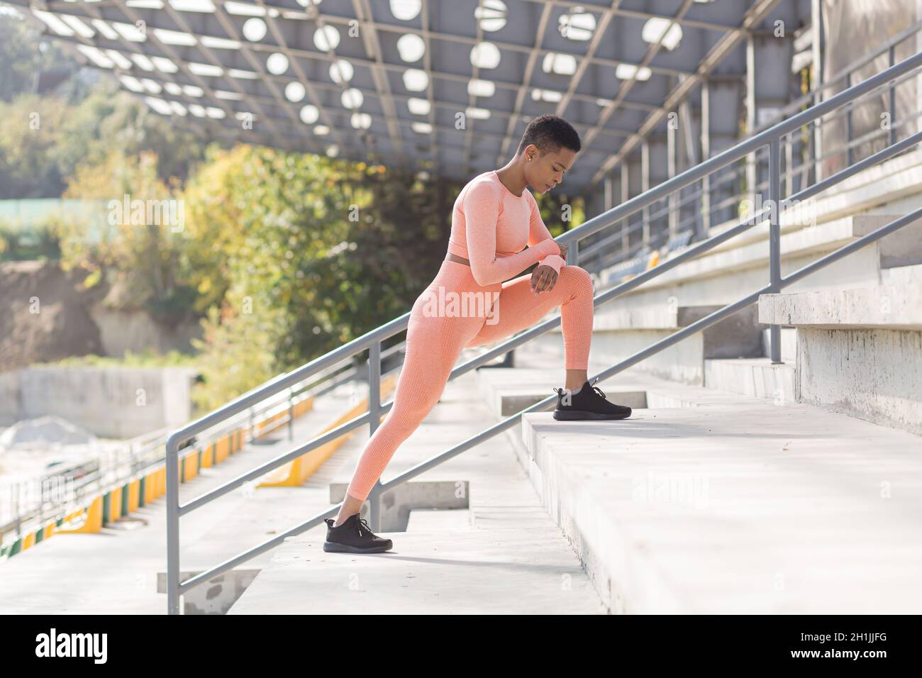 Female athlete doing fitness in a pink sports suit near the sports stadium, African American performs fitness exercises and stretching in the morning Stock Photo