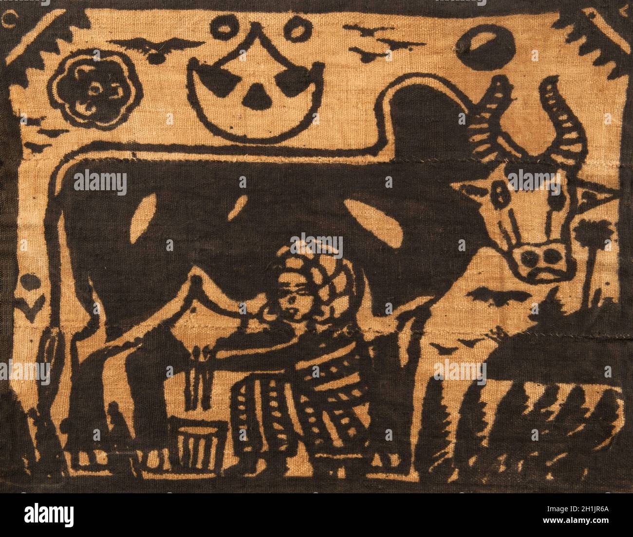 Traditional mud cloth, now called Bogolanfini depicting a figure of a woman milking a cow. The use of mud as a painting pattern on cotton is typical of the Bamana (Bamara) of Mali, centred on the Beledougou area north and northeast of Bamako. Women spin the locally-grown cotton, then men weave long bands that are joined together. The design of a Bogolanfini is traditionally made by women, though this cloth was made to sell to tourists and was made by a boy. Stock Photo