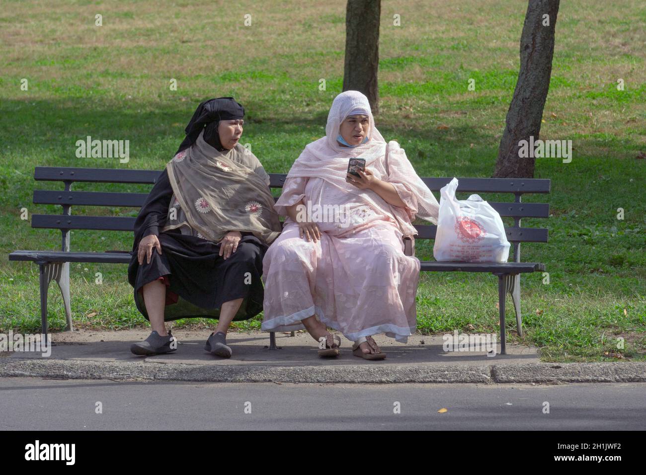 2 Muslim women in traditional clothing share aa bench  in Flushing Meadows Corona Park, Queens, New York City. Stock Photo