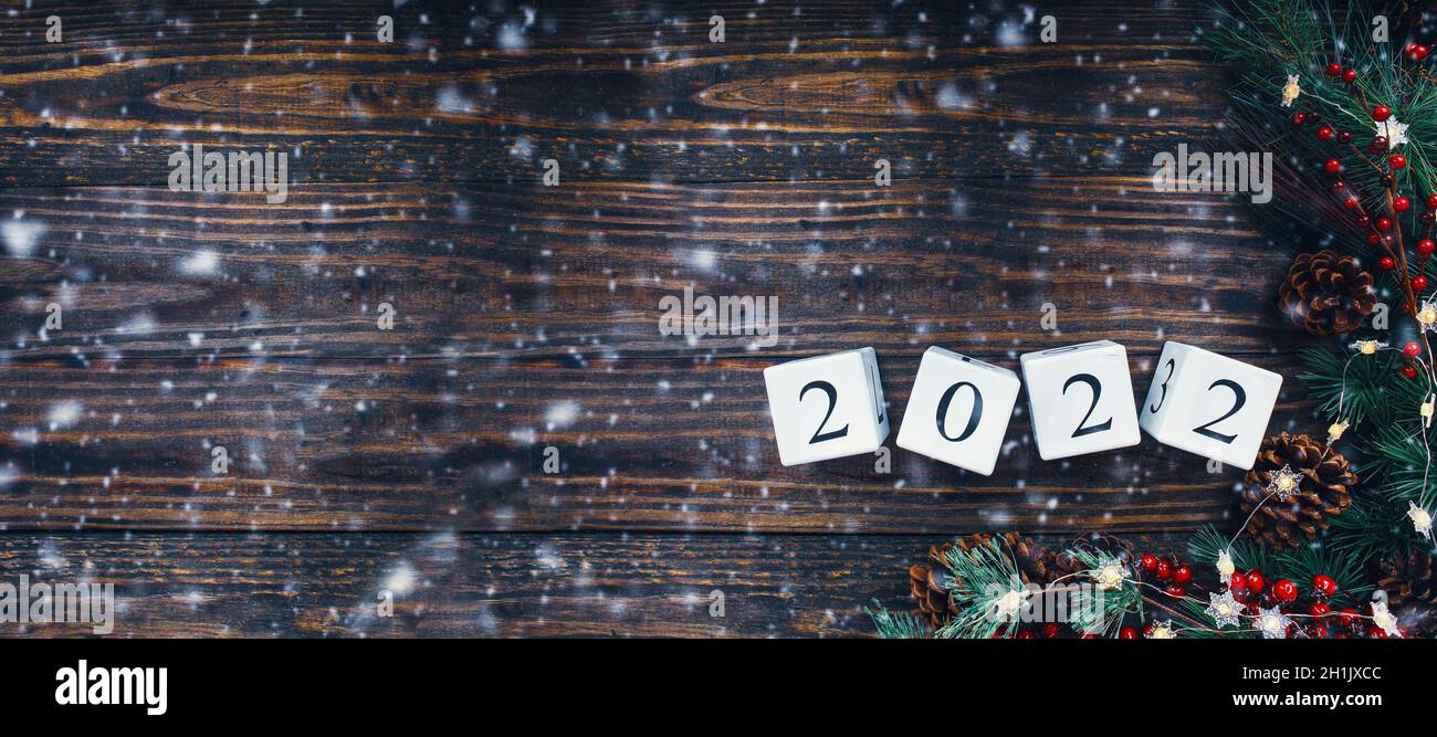 New Year's 2022 wood calendar blocks banner. Christmas tree lights, pine branches, red winter berries and snow. Top view with copy space available. Stock Photo