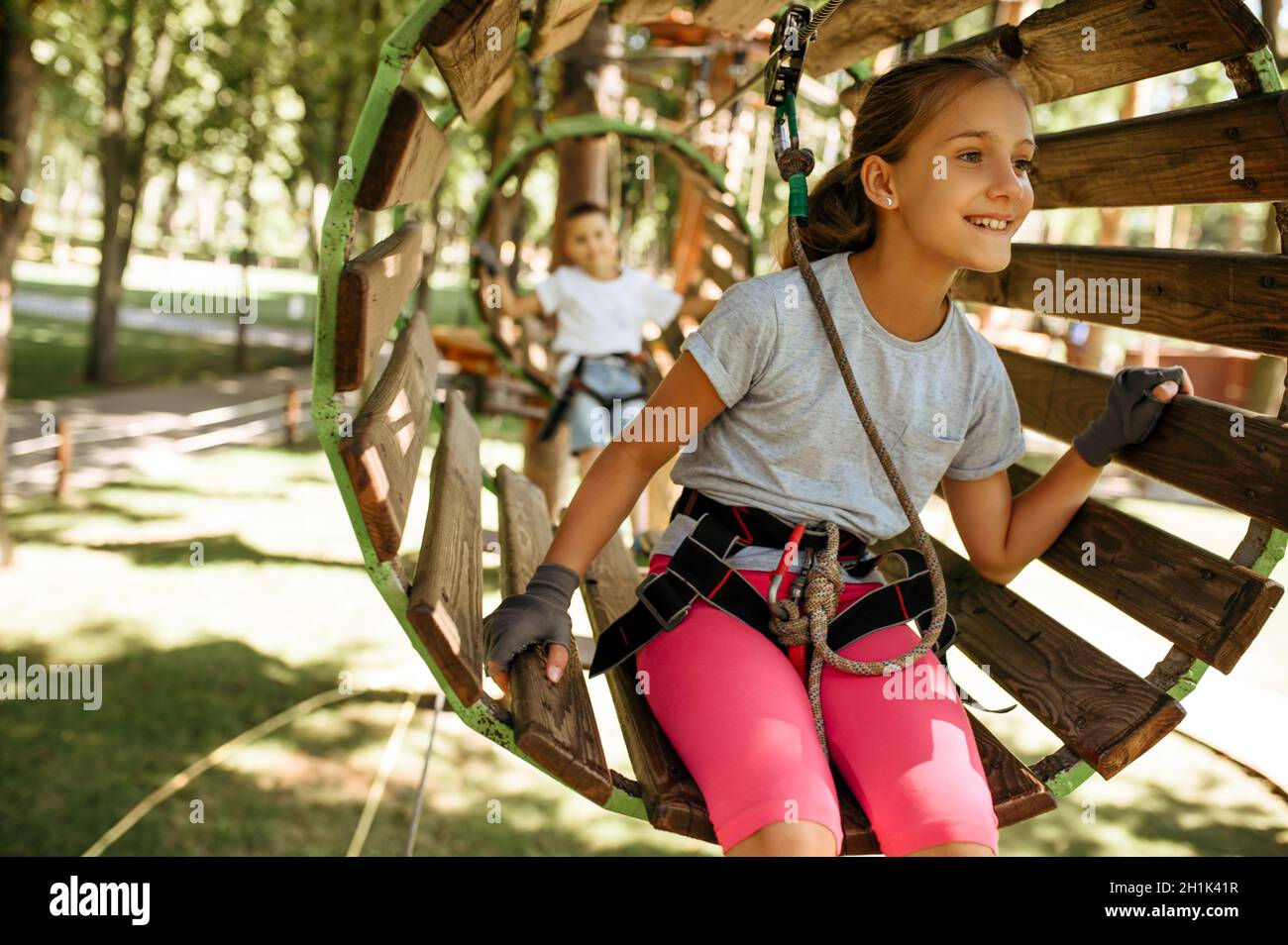 Smiling kids in equipment climbs in rope park, playground. Children climbing on suspension bridge, extreme sport adventure on vacations, danger entert Stock Photo