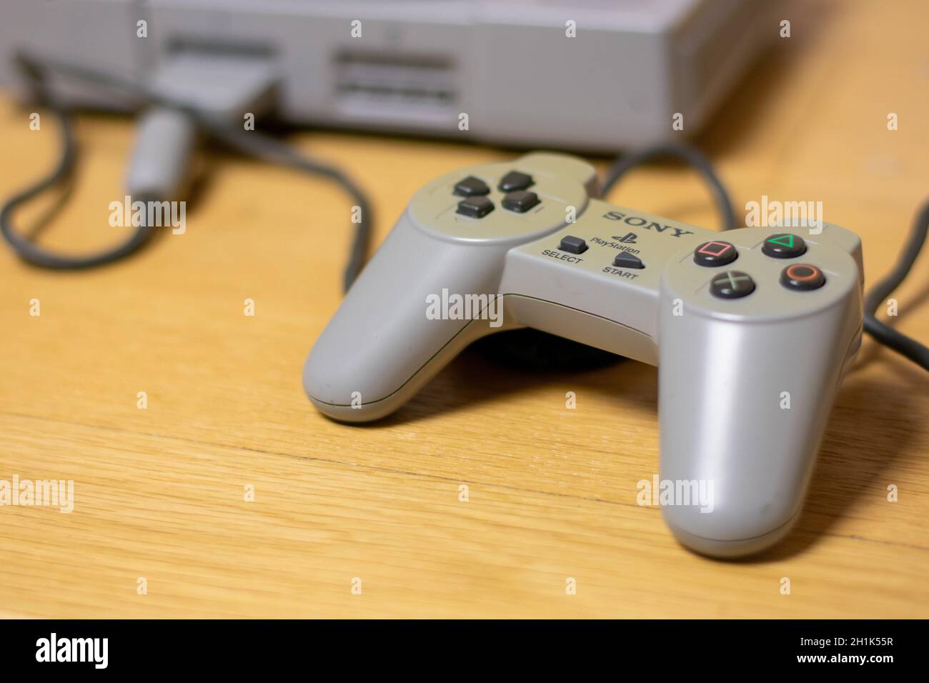 A Controller for the Original Playstation, Plugged Into the Console, on a wood floor. Stock Photo