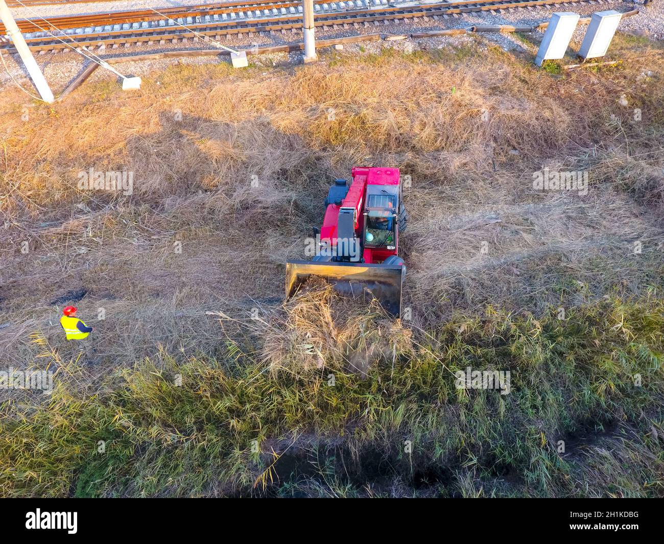 The bulldozer clears the space along the railway tracks. Raking of reeds by bulldozer. Stock Photo