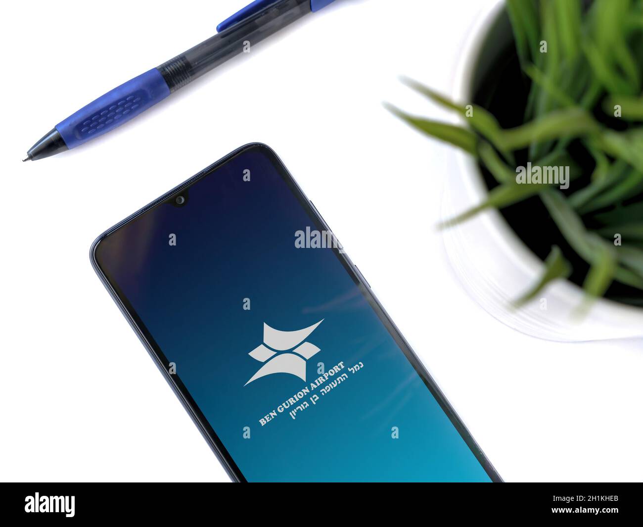 Lod, Israel - July 8, 2020: Modern minimalist office workspace with black mobile smartphone with Ben Gurion Airport app launch screen with logo on whi Stock Photo