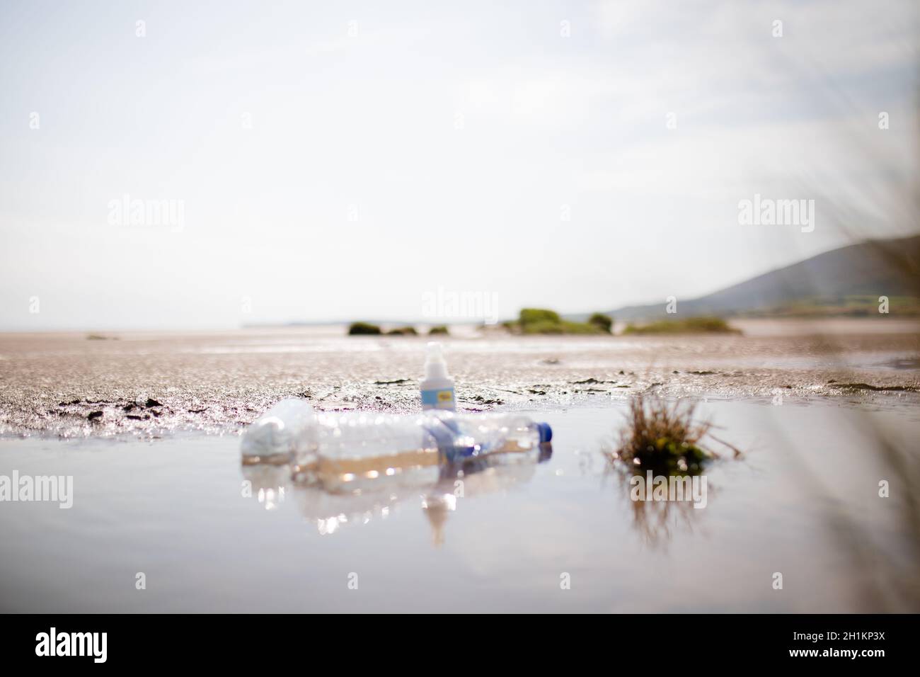Lanscape view of a couple of empty plastic bottles on a puddle in the sand with the clear blue sky as background Stock Photo