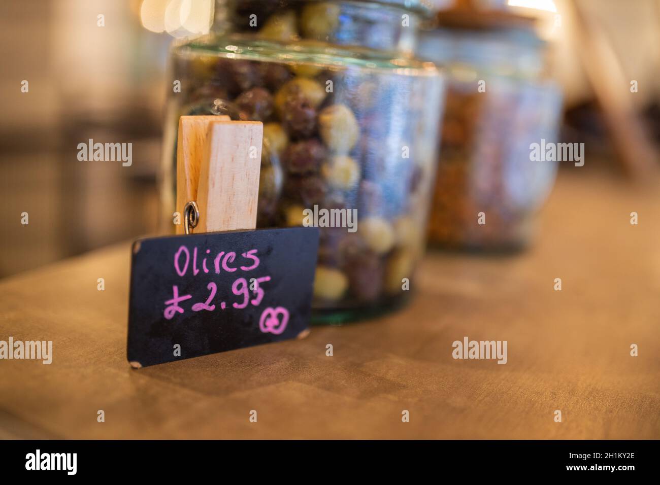 Picture of a price tag for olives next to a glass jar of dehydrated olives on the wooden counter of a vegan restaurant with a blurry background Stock Photo