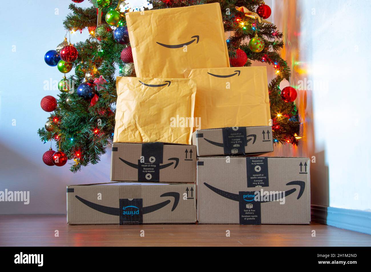 Calgary, Alberta, Canada. Nov. 16, 2020. Amazon boxes and envelopes under a Christmas tree with ornaments and lights on. Concept: Delivering packages Stock Photo