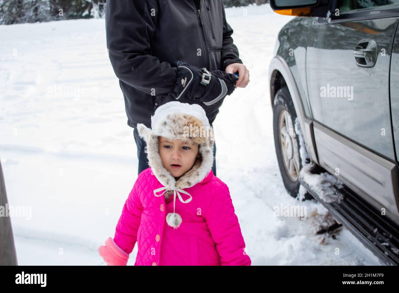 Concerned little girl wearing pink coat and standing next to a truck in ...