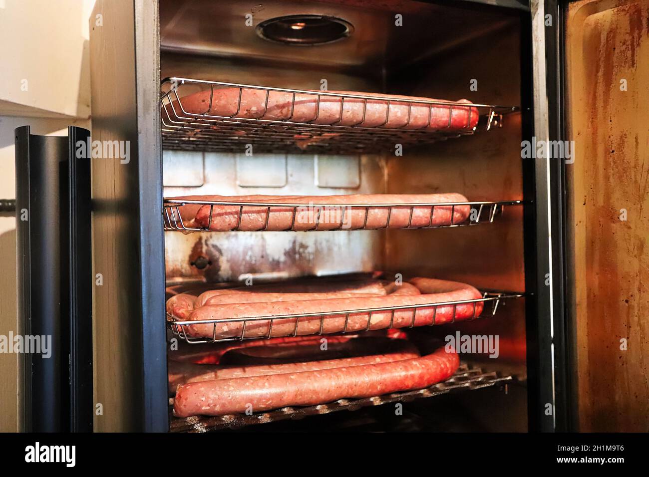 Four trays of sausage in a smoker with the door open. Stock Photo