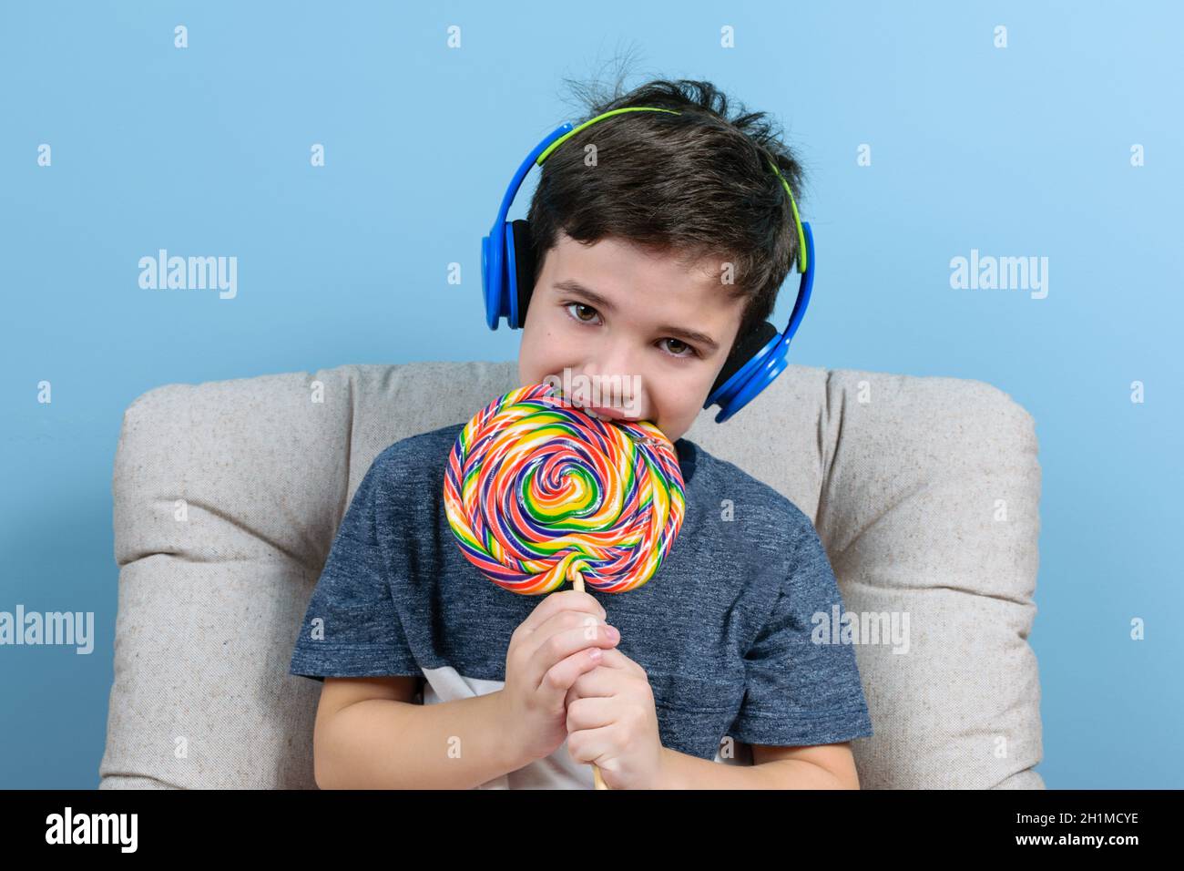 8 year old child with headphone and biting a big colorful lollipop. Stock Photo