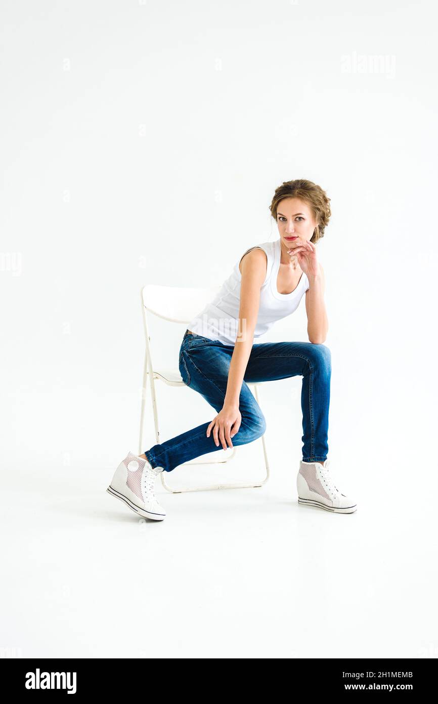 cheerful girl in a white t-shirt and dark blue jeans in the studio on a white background stands, sits, runs Stock Photo