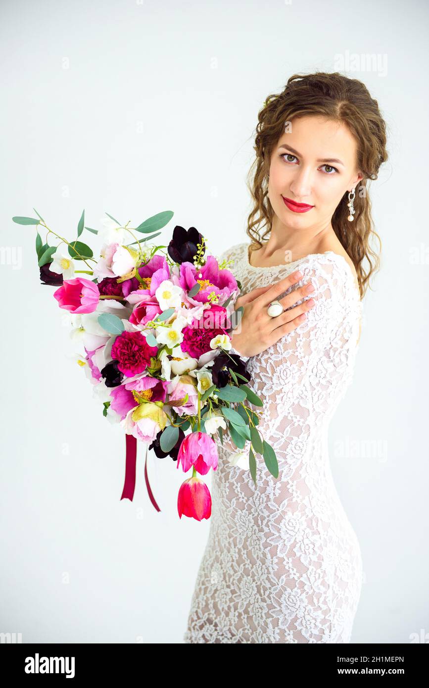 joyful girl bride in a white knitted dress posing with a bouquet of flowers in the studio on a white background Stock Photo