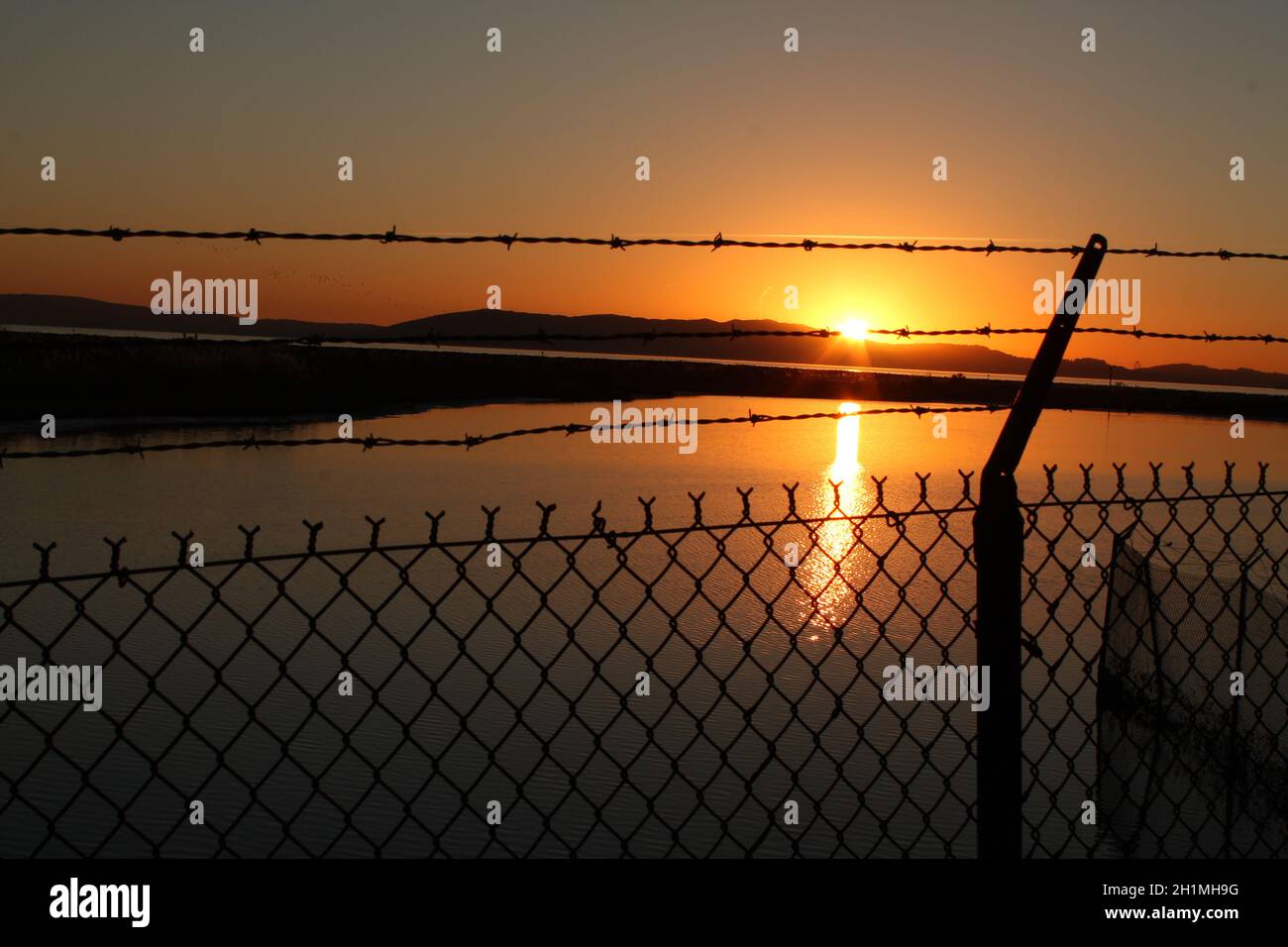 Red sunset over water through barbed wire fence Stock Photo - Alamy