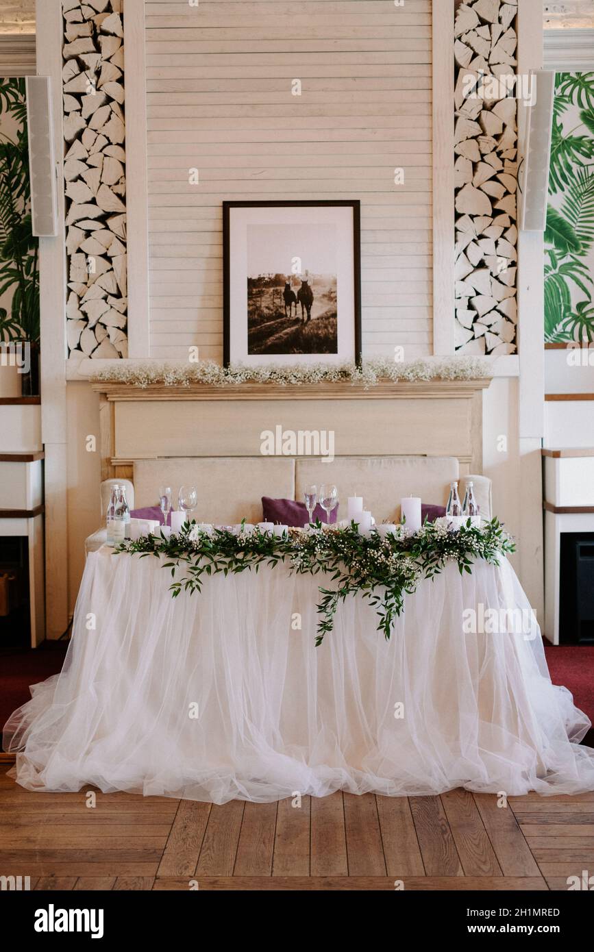 the presidium of the newlyweds in the banquet hall of the restaurant is decorated with candles and green plants, the general tone of the hall is beige Stock Photo