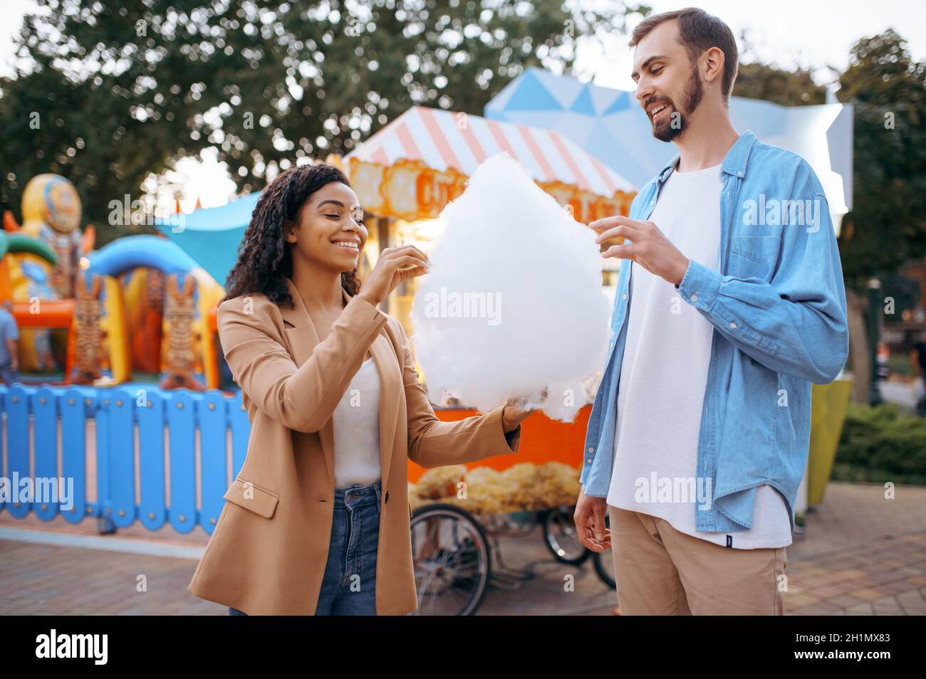 Love couple eating cotton candy in city amusement park. Man and woman relax outdoors. Family leisures in summertime, entertainment theme Stock Photo