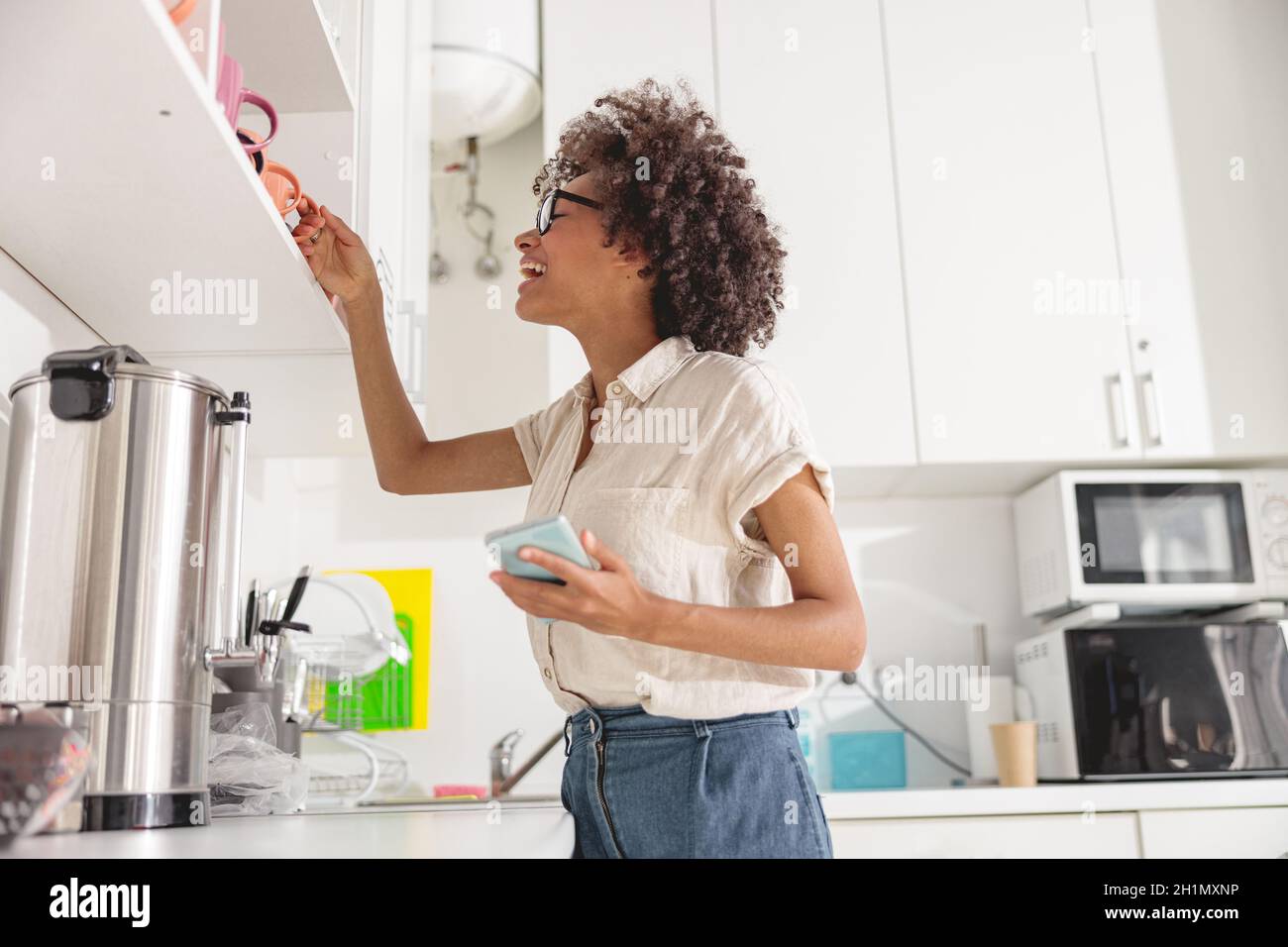 Pretty young woman taking a cup off the shelf Stock Photo